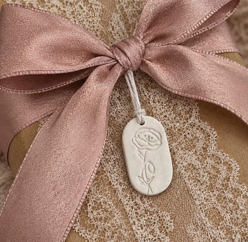 A small oval shaped gift tag handmade from air dry clay. The tag is stamped with a poppy flower representing the birth flower for August .  the gift tag can be purchased with a cotton drawstring bag . other items are available to match.