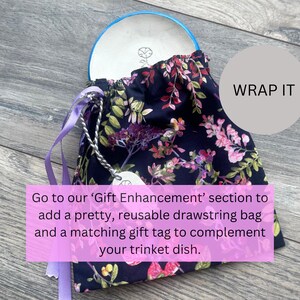 May include: A navy blue drawstring bag with a floral pattern, holding a white trinket dish with a blue rim. The bag has purple ribbons and a silver chain with a tag. Text on the image says "WRAP IT".