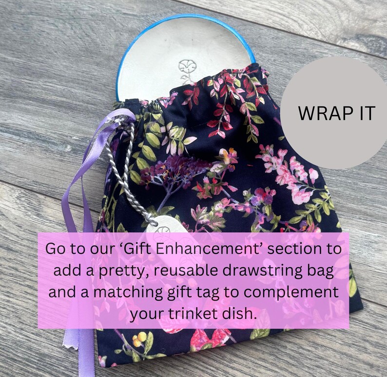 May include: A navy blue drawstring bag with a floral pattern, holding a white trinket dish with a blue rim. The bag has purple ribbons and a silver chain with a tag. Text on the image says "WRAP IT".