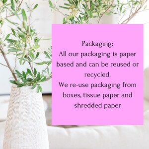 May include: A white textured vase containing green leafy branches next to a bright pink square sign with black text that reads: Packaging: All our packaging is paper based and can be reused or recycled. We re-use packaging from boxes, tissue paper and shredded paper.