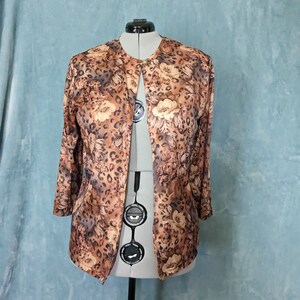 May include: A brown and beige patterned cardigan with a floral and leopard print. The cardigan has a long sleeve and a button closure.