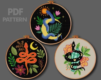 May include: Three cross-stitch patterns in wooden hoops. The designs feature snakes, moons, flowers, and crystals. The top design has a blue snake around a yellow crescent moon. The text "PDF PATTERN" is in the upper left corner.