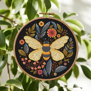 May include: A cross-stitch embroidery hoop featuring a bee design. The bee has yellow wings and a black and yellow striped body, surrounded by colorful flowers and leaves on a black background. The wooden hoop is visible.