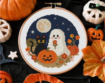 Op de afbeelding: Een borduurring met een Halloween-ontwerp. Het ontwerp toont een zwarte kat, een spook met een bloem, een pompoen en een volle maan tegen een donkerblauwe sterrenhemel. De ring is omgeven door pompoenen en andere Halloween-decoraties.