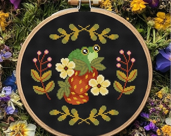 May include: A cross-stitch embroidery hoop with a green frog on a strawberry, with yellow flowers and foliage on a black background. The design is framed in a wooden hoop, a charming piece of textile art.