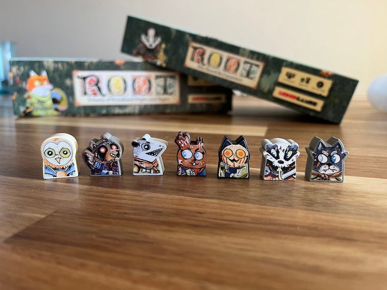 May include: Eight different Root game character pieces, each with a unique animal design. The pieces are made of plastic and have a white base with a colorful animal illustration on the front. The pieces are arranged in a row on a wooden surface.