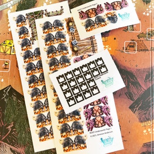 May include: A set of stickers for the Root board game. The stickers are printed on white paper and feature various designs, including crowns, a character with a helmet, and a creature with wings. The stickers are labeled "ROOT Underworld Page 1" and "ROOT Underworld Crowns".