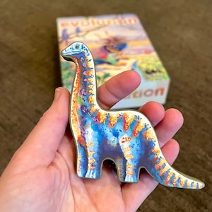 May include: A blue, orange, and yellow dinosaur toy with a long neck and tail. The toy is made of wood and has a painted finish.