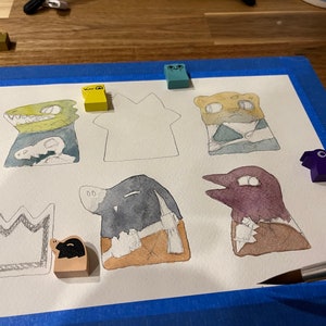 May include: A watercolor painting of various animal characters on a white background. The characters include a crocodile, a cheetah, a bird, a pig, and a house. The painting is surrounded by blue painter's tape.