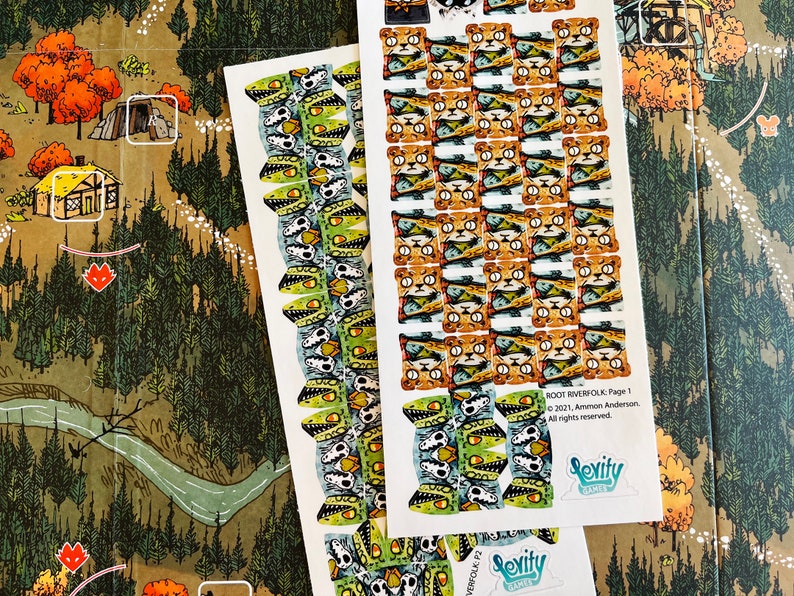 May include: Two sheets of stickers for the board game Root Riverfolk. The stickers are printed on white paper and feature illustrations of various creatures, including a cat-like creature with a fish in its mouth and a skull-like creature with a green and white design. The text on the sheet reads "ROOT RIVERFOLK: Page 1" and "2021, Ammon Anderson. All rights reserved."