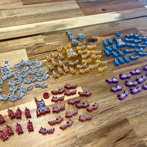 May include: A collection of game pieces in various colors, including white, gray, yellow, red, blue, and purple. The pieces are arranged in rows on a wooden surface.