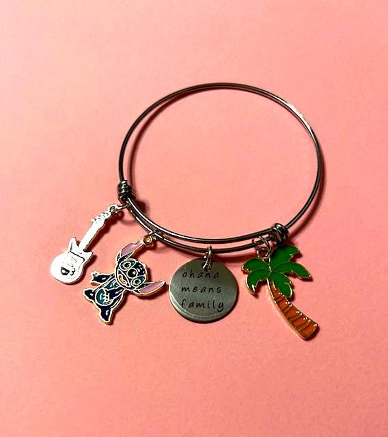 Puede incluir: Un brazalete de plata con un personaje azul Stitch, un dije de palmera, un dije de guitarra y un dije redondo que dice "ohana means family".
