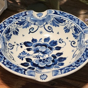 May include: A white ceramic ashtray with a blue and white floral design. The ashtray has a scalloped edge and a wide, shallow bowl.