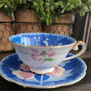 May include: A blue and white teacup and saucer set with a floral design. The cup has a gold rim and the saucer has a scalloped edge.