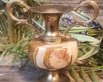 May include: A small, gold-toned, marble vase with ornate handles. The vase has a brown, white, and pink marbled pattern.