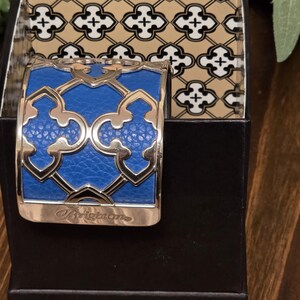 Pu&ograve; includere: Un bracciale a polsino blu e argento con un design geometrico, presentato in una scatola nera. Il bracciale presenta un centro blu strutturato e dettagli argentati. La scatola ha un interno a fantasia. La parola "Brighton" &egrave; incisa sul bracciale.