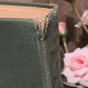 Op de afbeelding: Close-up van een vintage boek getiteld "The Sea Fairies" van L. Frank Baum. Het boek heeft een versleten, donkergroene kaft met zichtbare slijtage aan de hoeken. De pagina's zijn vergeeld en de titel is gedeeltelijk zichtbaar.