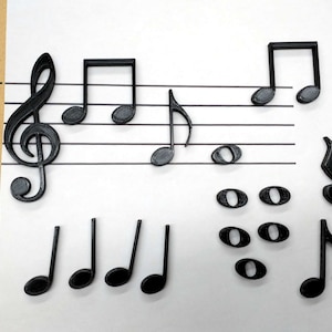 May include: A set of black plastic musical note magnets, including a treble clef, quarter notes, eighth notes, and a set of four sixteenth notes. The magnets are 1.75 inches tall and are arranged on a white sheet of paper with five lines.