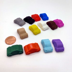 May include: A set of 12 miniature toy cars in various colors, including red, blue, green, yellow, purple, brown, white, black, orange, and gray. The cars are all the same size and shape, and they are arranged in a row on a white surface.