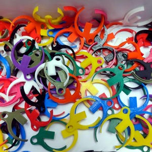 Puede incluir: Una colección de abalorios de plástico de colores en forma de una letra 'S' estilizada con un lazo en la parte superior. Los abalorios son de varios colores, incluyendo rojo, azul, verde, amarillo y blanco.