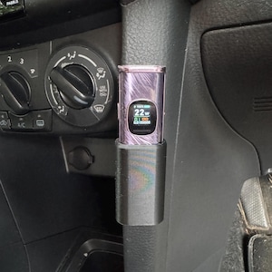 Puede incluir: Un bolígrafo de vapeo negro y morado con una pantalla digital que muestra 22w y 100% de batería. El bolígrafo de vapeo está en un soporte negro montado en un coche.