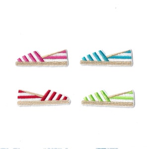May include: Four embroidered patches shaped like slip-on shoes, each featuring a distinct color of diagonal stripes: pink, blue, red, and green. Every patch includes a tan-colored base representing a jute sole and white fabric accents.