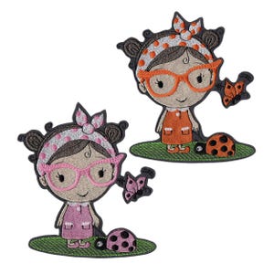 Op de afbeelding: Twee geborduurde patches met cartoonmeisjes met brillen, haarbanden en jurken. Het ene meisje draagt een oranje jurk en een oranje bril, het andere een roze jurk en een roze bril. Elke patch bevat een vlinder en een lieveheersbeestje.