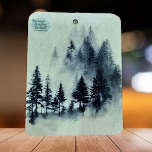 May include: Rectangular air freshener with a misty forest scene in shades of gray and black. The air freshener has a small hole at the top for hanging and the text "Soap Freakin' Excited!" in a circular logo.