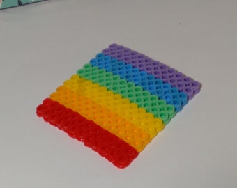 Op de afbeelding: Een vierkant gemaakt van kleine plastic kralen, gerangschikt in rijen om een regenboogpatroon te creëren. De kralen zijn rood aan de onderkant en paars aan de bovenkant.