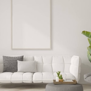 Könnte beinhalten: Ein weißes Sofa mit grauen Kissen steht in einem modernen Wohnzimmer mit einem grauen Sessel, einer Topfpflanze und einer Stehlampe. Ein gerahmtes Bild hängt an der Wand hinter dem Sofa.