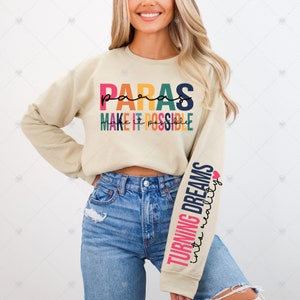 May include: A beige sweatshirt with the text "paras make it possible" in rainbow colors on the front. The left sleeve has the text "turning dreams into reality" in rainbow colors with a small pink heart.