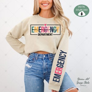 Puede incluir: Una sudadera beige con el texto "EMERGENCY DEPARTMENT" en una fuente de bloque colorida con un pequeño corazón rosa sobre el texto. La manga derecha tiene la palabra "EMERGENCY" en una fuente de bloque colorida vertical.