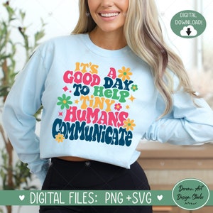 May include: Light blue long-sleeve shirt with the text "IT'S A GOOD DAY TO HELP TINY HUMANS COMMUNICATE" in colorful retro font. The design includes flowers and stars. Digital download available.