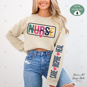 May include: A beige sweatshirt with the word "NURSE" in colorful letters and a heart on the front. The left sleeve has the words "CARE INSPIRE HEAL" with hearts in between each word.