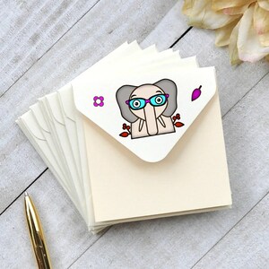 May include: A stack of ivory note cards with a cute cartoon elephant wearing pink glasses and a red flower on the front.