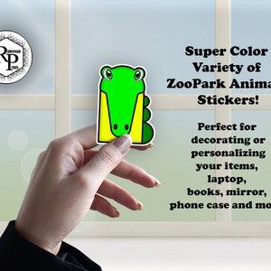 May include: A green alligator sticker with yellow accents. The sticker is being held by a hand. The text "Super Color Variety of ZooPark Animals Stickers!" is written in black text on a white background. The text "Perfect for decorating or personalizing your items, laptop, books, mirror, phone case and more!" is written in black text on a white background.
