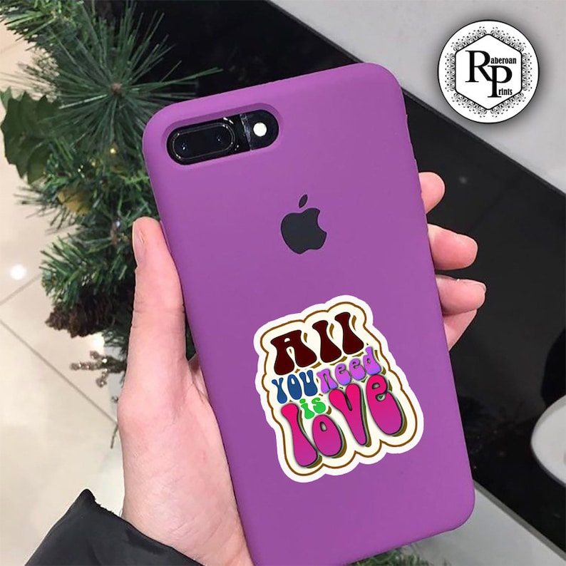 May include: Purple phone case with a sticker that says "All you need is love" in a retro font with colorful letters.