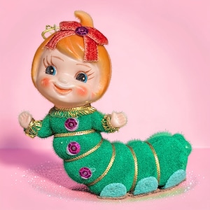 May include: A vintage-style figurine of a caterpillar with a human-like face, featuring orange hair topped with a red velvet bow and a purple sequin. The body is covered in green felt with gold trim, purple sequins, and light blue feet.