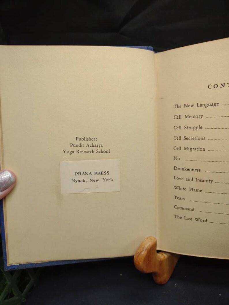 May include: Open book with text, held open by a wooden book stand. The left page displays the publisher's information: PRANA PRESS, Nyack, New York. The right page lists the table of contents, including "Cell Memory" and "White Flame."