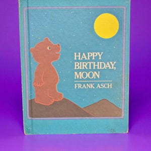May include: A children's book titled "Happy Birthday, Moon" by Frank Asch. The cover features a brown bear, a yellow moon, and text on a blue background. The book is rectangular and has a light blue border.