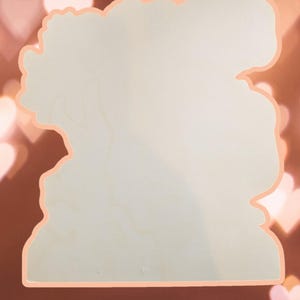 May include: Blank wooden cutout in the shape of a woman's head with a floral design around the edges. The cutout is a light beige color and has a smooth surface.