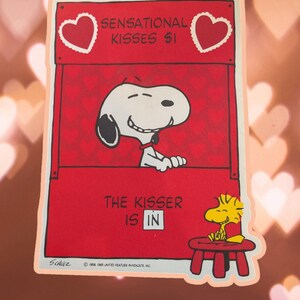 May include: A red and white vintage Valentine's Day card featuring Snoopy, the beloved beagle from Peanuts, peeking out of a booth with the text "Sensational Kisses $1".  Snoopy is smiling and has a heart-shaped nose.  Woodstock, Snoopy's yellow bird friend, is sitting on a red stool with a piece of paper in his beak.