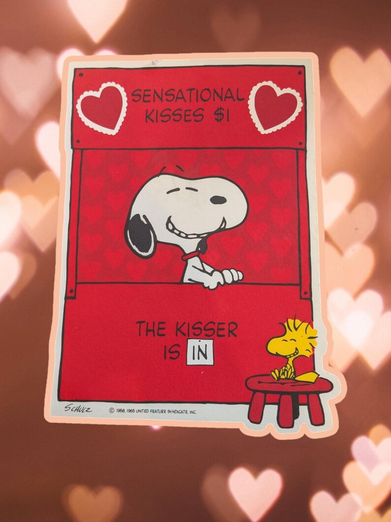 May include: A red and white vintage Valentine's Day card featuring Snoopy, the beloved beagle from Peanuts, peeking out of a booth with the text "Sensational Kisses $1".  Snoopy is smiling and has a heart-shaped nose.  Woodstock, Snoopy's yellow bird friend, is sitting on a red stool with a piece of paper in his beak.
