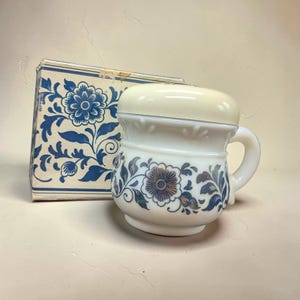 May include: A white ceramic shaving mug with a matching lid and handle, decorated with blue floral patterns. A matching box with blue floral designs is visible in the background. The mug has a vintage aesthetic.