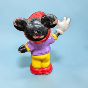 Op de afbeelding: Een vintage Mickey Mouse beeldje, met een rode hoed, zwarte oren en een paars shirt. Het beeldje heeft een gele broek, rode schoenen en witte handschoenen. Het beeldje staat met &eacute;&eacute;n arm omhoog.
