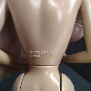 Peut inclure: Gros plan de l'arri&egrave;re d'une poup&eacute;e en plastique de couleur chair avec le texte "&copy;MATTEL, INC. 1988 TAIWAN" imprim&eacute; sur le bas du dos.