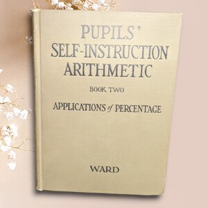 May include: A vintage book titled "Pupils' Self-Instruction Arithmetic Book Two: Applications of Percentage" by Ward. The book has a beige cover with black lettering.