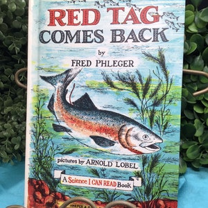 May include: Vintage children's book titled "RED TAG COMES BACK" by Fred Phleger, with illustrations by Arnold Lobel. The cover features a colorful illustration of a fish in water. The book is part of the "A Science I CAN READ Book" series.