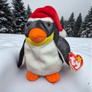 May include: A plush penguin toy wearing a red Santa hat with a white trim and a white pom-pom. The penguin has a black head and wings, a white belly, and orange feet and beak. A heart-shaped tag is attached to the penguin.