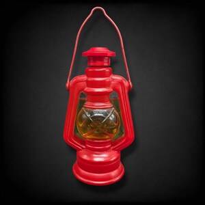 May include: A red lantern with a handle, featuring a clear, round glass section containing a yellow liquid. The lantern has a classic design with a base, a top, and a handle for carrying. The background is black.